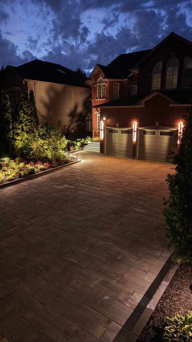 Interlocking driveway lit at dusk with garden uplighting